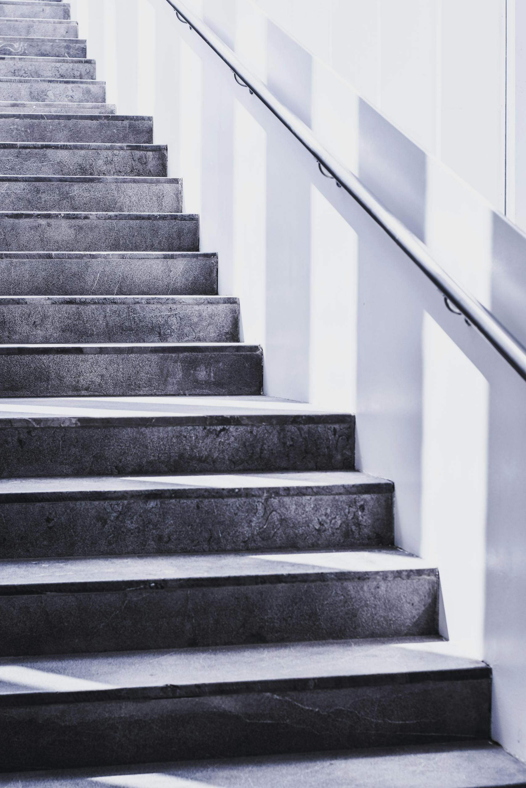 A contemporary concrete staircase with sleek steel railing and natural light casting shadows.