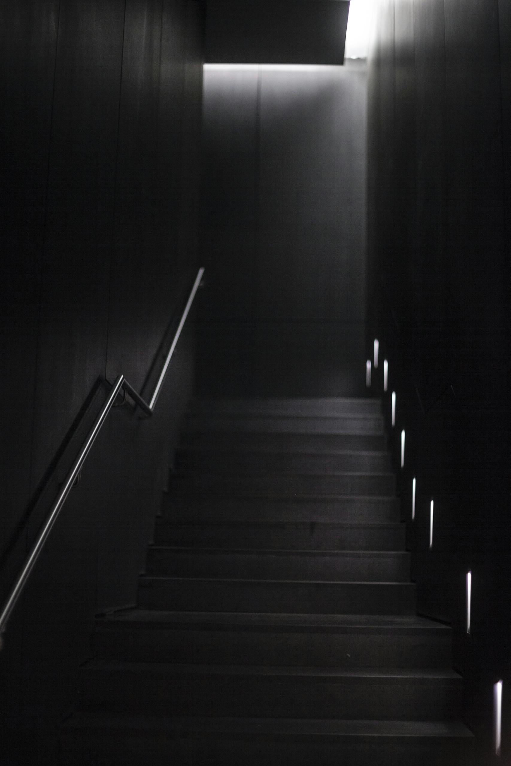 A modern, dimly lit staircase with minimalist design seen from below, featuring sleek walls and subtle lighting.